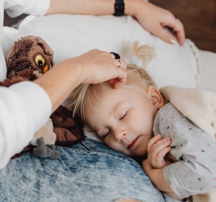A mother gently strokes her sleeping child's hair as they snuggle indoors, creating a warm family moment.