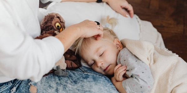 A mother gently strokes her sleeping child's hair as they snuggle indoors, creating a warm family moment.